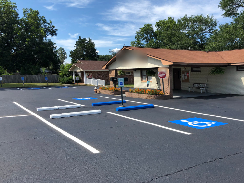 After: the same lot sealed black with fresh white stall lines, blue wheel stops and a blue ADA space