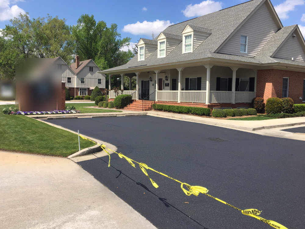 After: the same entrance drive sealed a deep, even black, with caution tape keeping traffic off while it cures