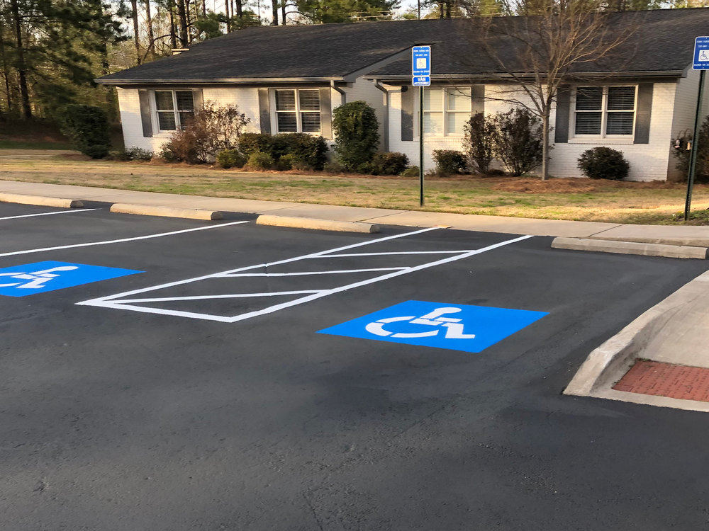 After: the same lot sealed black with bright blue accessible spaces and a white striped access aisle
