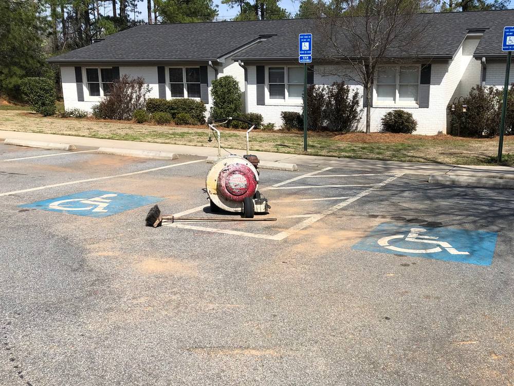 Before: worn, sandy gray parking lot with faded accessible-parking symbols beside a curb ramp