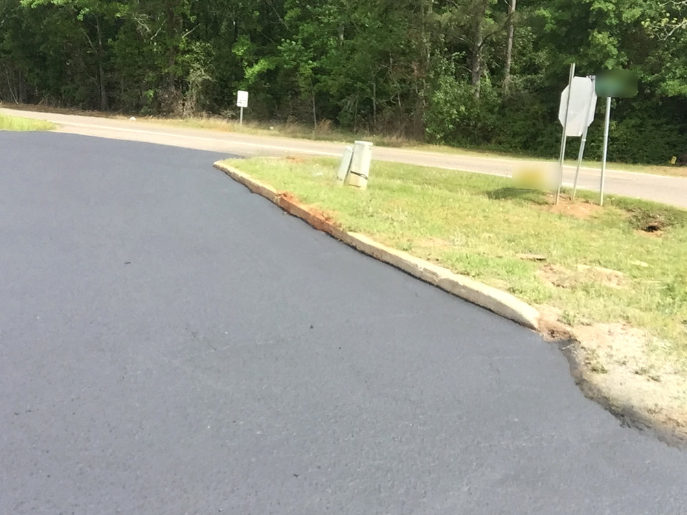 After: the same drive apron sealed smooth and black along the curb and grass