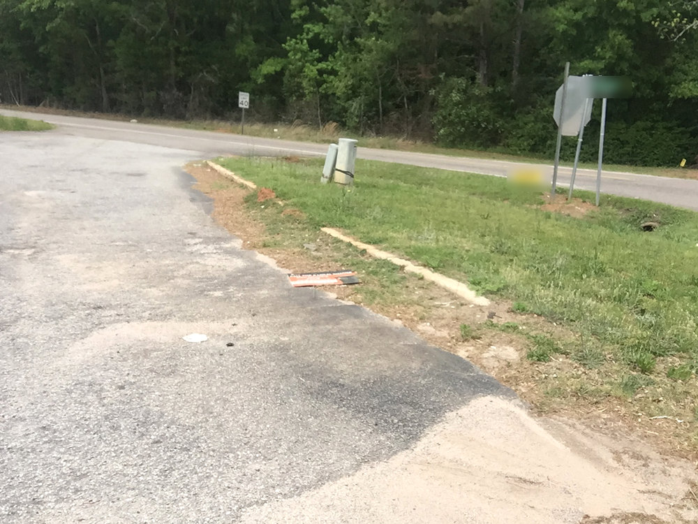 Before: cracked, patched gray drive apron meeting a country road, with sand along the edge