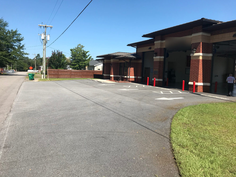 Before: gray, weathered parking area in front of a brick building with large bay doors